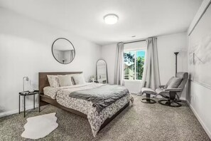 A bedroom with a bed, a chair, a round mirror, and a window with curtains. - Family Vacation Home - DWTN - Airhockey - Spacious (Vancouver)