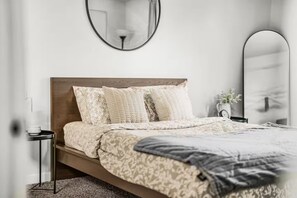 A bedroom with a wooden headboard, a patterned bedspread, and a bedside table with a lamp. - Family Vacation Home - DWTN - Airhockey - Spacious (Vancouver)