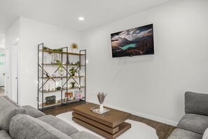 Un salon moderne avec un canapé, une table basse, une bibliothèque et un tableau représentant un paysage, accroché au mur.