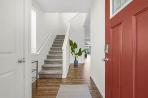 A hallway with a staircase leading to a second floor, a red door, and a potted plant. - Family Vacation Home - DWTN - Airhockey - Spacious (Vancouver)