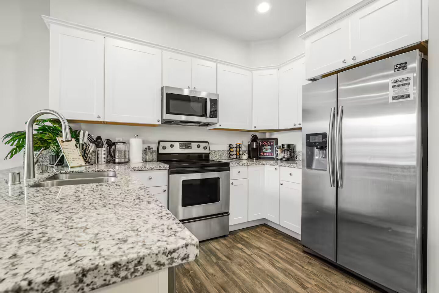 A modern kitchen with white cabinets, stainless steel appliances, granite countertops, and a wooden floor.