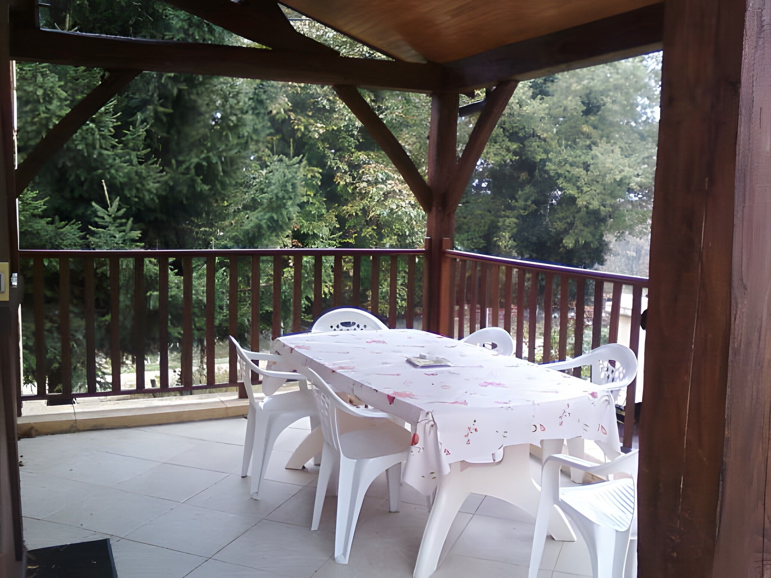 Een terras buiten met een tafel en stoelen, omringd door een houten hek, met uitzicht op een bebost gebied.
