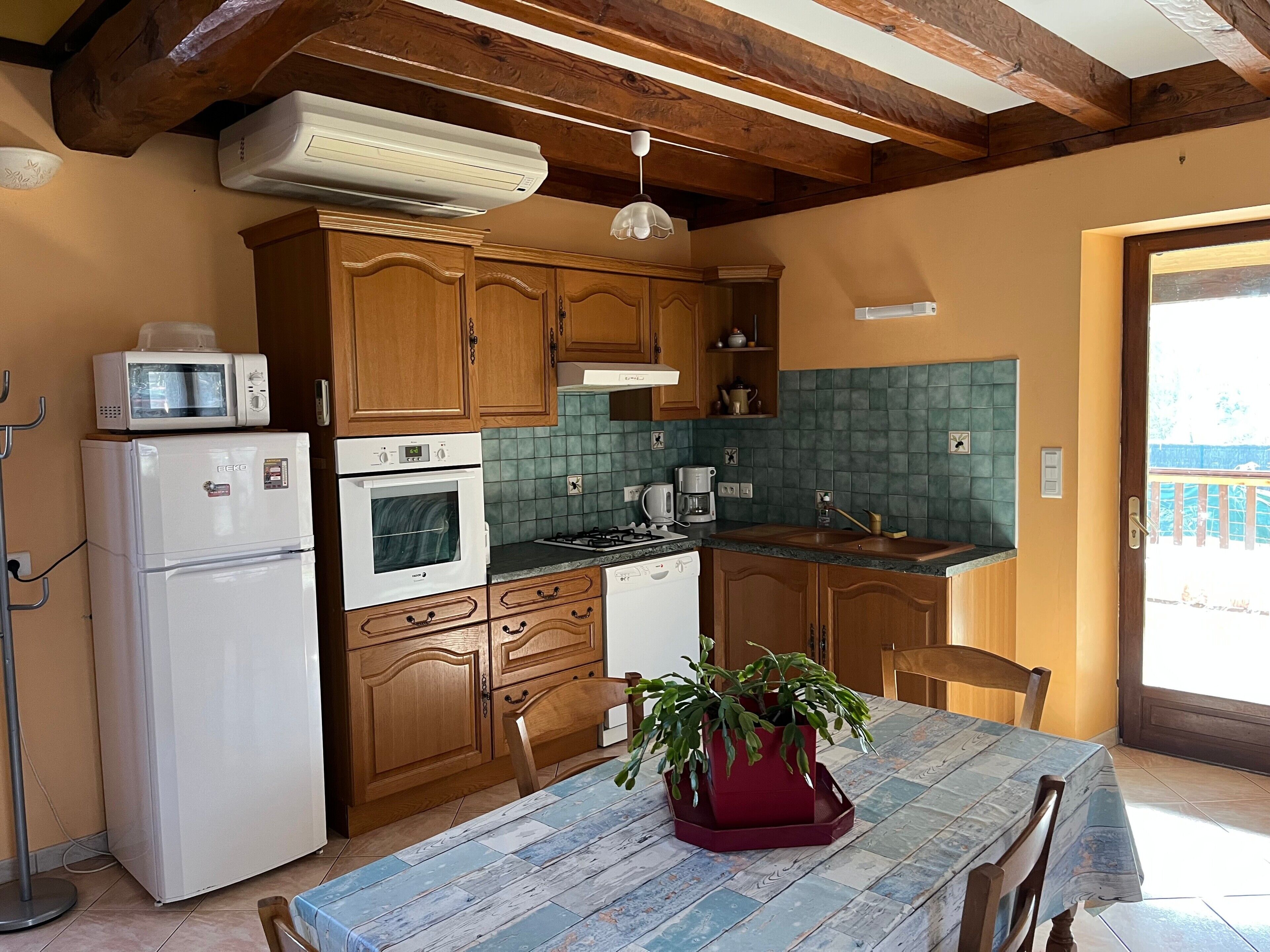 Une cuisine avec des meubles en bois, un four à micro-ondes, un réfrigérateur, un four traditionnel, un évier et une table à manger agrémentée d’une plante.