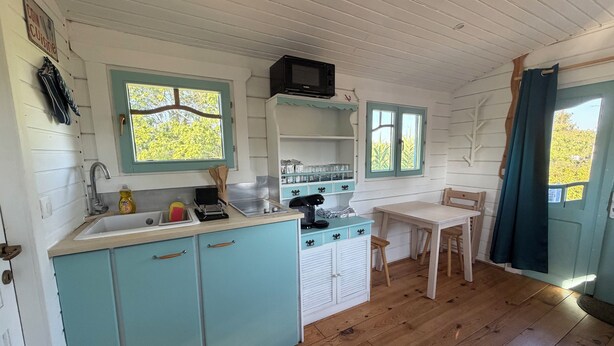 Ett kompakt kök med diskho, spis och mikrovågsugn. Det finns skåp, ett bord och stolar.