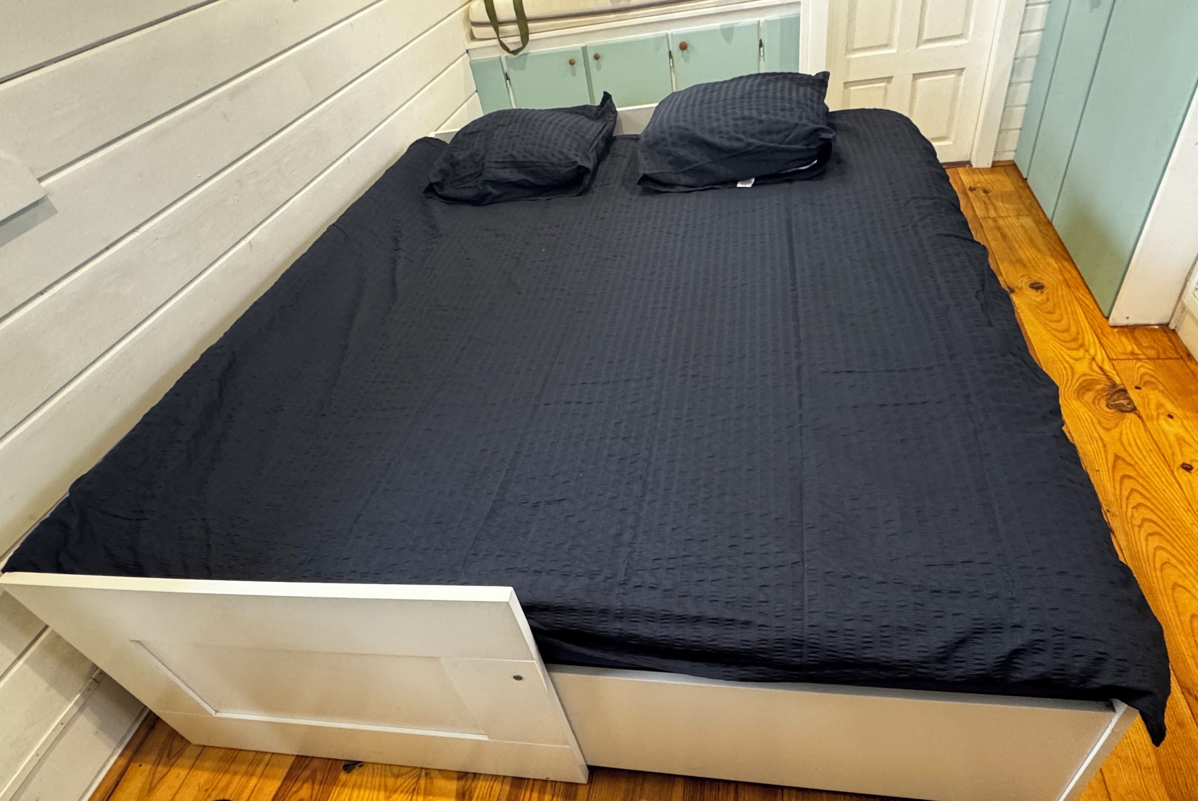Een eenpersoonsbed met een wit frame en een zwarte matras, voorzien van twee kussens.