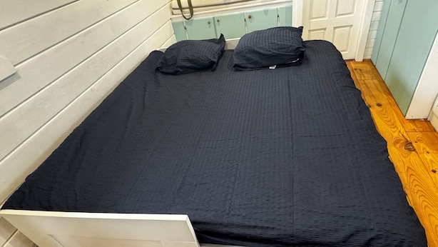 Ein Einzelbett mit weißem Gestell und einer schwarzen Matratze, ergänzt durch zwei Kissen.