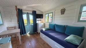 Ett mysigt rum med trägolv, en soffa med turkosa kuddar, ett litet bord och en stol.
