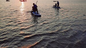 Água calma com pessoas em pranchas de remo ao pôr do sol.