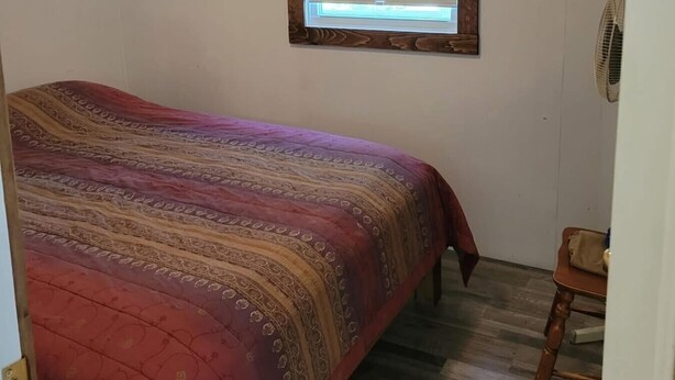 Um quarto com uma cama, janela, ventilador e porta.