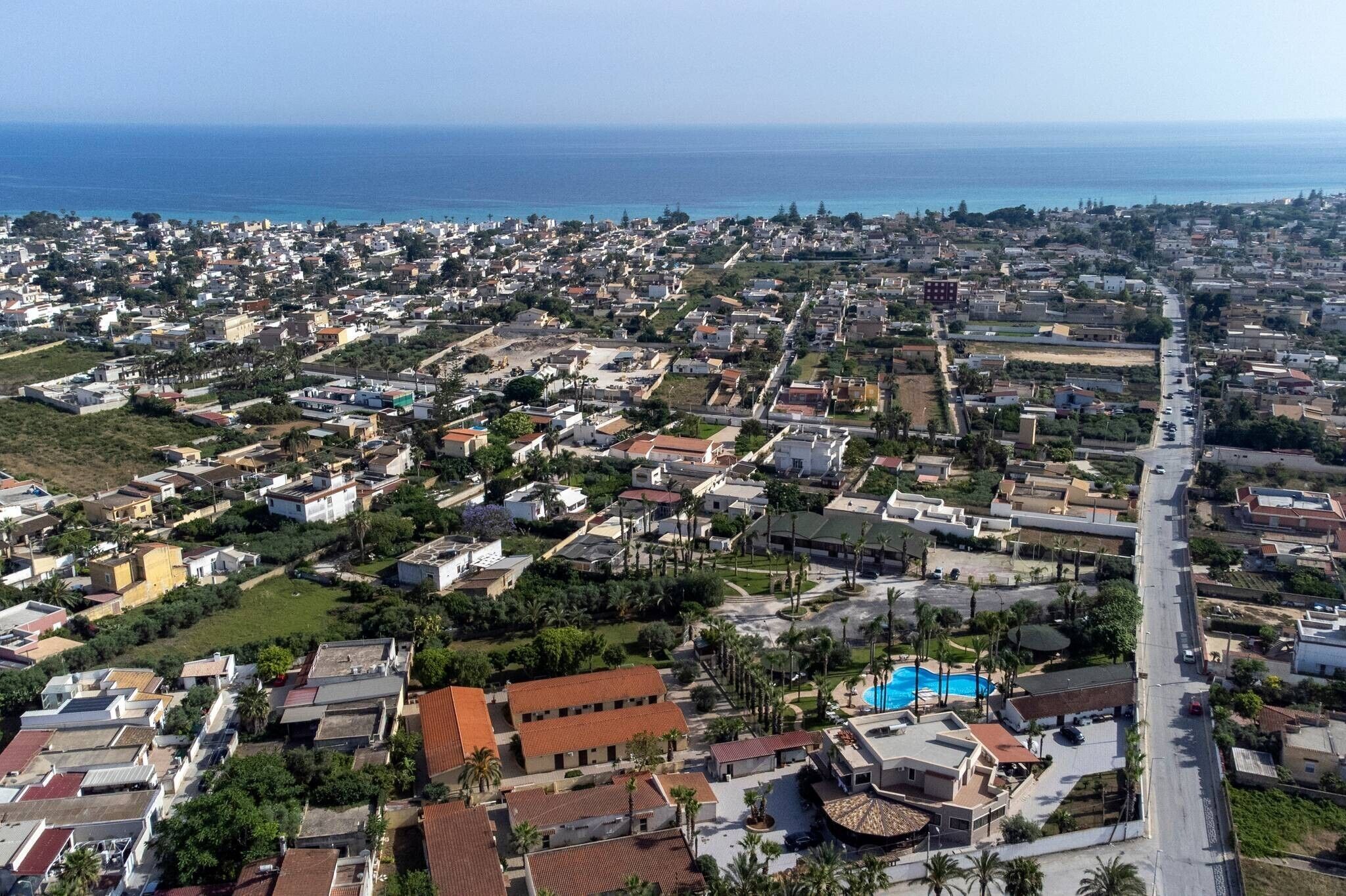 An aerial view of a coastal residential area with houses, a main road, and a swimming pool.
