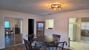 A dining area with a round table and chairs, a ceiling light fixture, and a view into another room with a refrigerator. - Lovely 2-bedroom house with AC in cool Port Richey (Port Richey)