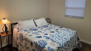 A bedroom with a bed, a nightstand, a lamp, a ceiling fan, and a window with blinds. - Lovely 2-bedroom house with AC in cool Port Richey (Port Richey)