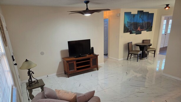 A living room with a sofa, a television on a wooden stand, a ceiling fan, and a dining area with a table and chairs. - Lovely 2-bedroom house with AC in cool Port Richey (Port Richey)