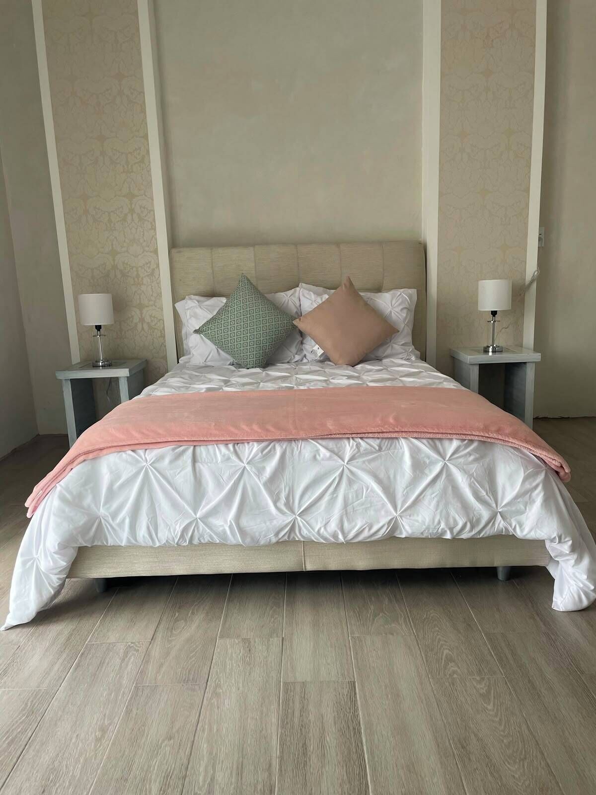 A neatly made bed with a patterned bedspread and pillows, two bedside tables with lamps, and a wooden floor.