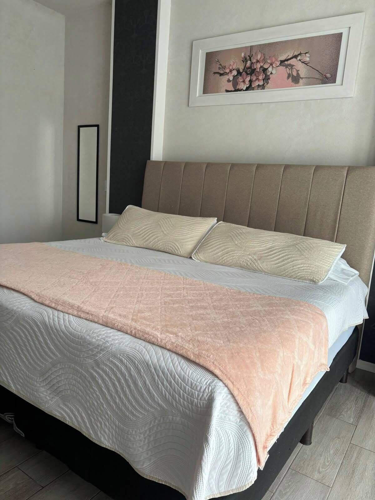 Una cama con cabecera, una mesita de noche y un cuadro colgado en la pared.
