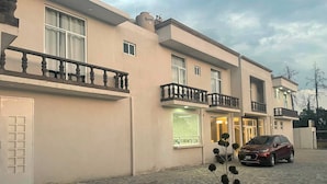 A multi-story building with a balcony, a potted plant, and a parked car. - Hotel Del Real (Tepotzotlán)