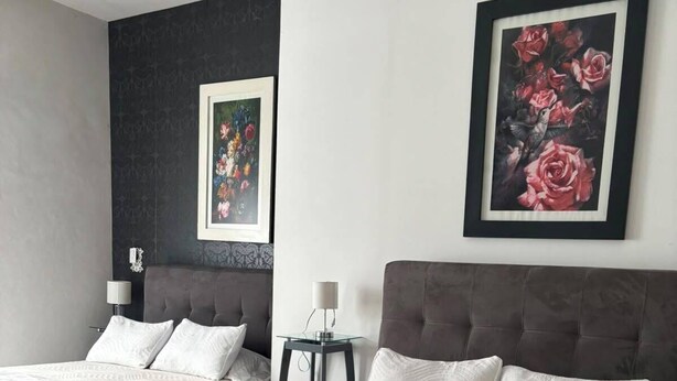 A hotel room with two beds, a small table, and two framed floral paintings on the walls. - Hotel Del Real (Tepotzotlán)