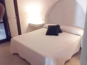 A single bed with a white bedspread and a black pillow in a room with a curved ceiling and a small bedside table. - villa Passione (Palau)