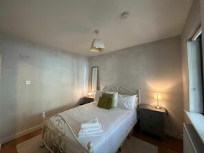 Ein Schlafzimmer mit Bett, Nachttisch, Lampe und einem Fenster.