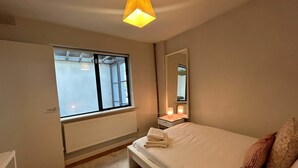 A bedroom with a bed, a window, a radiator, a bedside table with a lamp, and a mirror. - 2BDR 2BA Upside Down House with Sunny Balcony (Dublin)