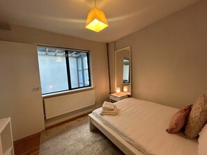 A bedroom with a bed, a window, a radiator, a bedside table with a lamp, and a mirror. - 2BDR 2BA Upside Down House with Sunny Balcony (Dublin)