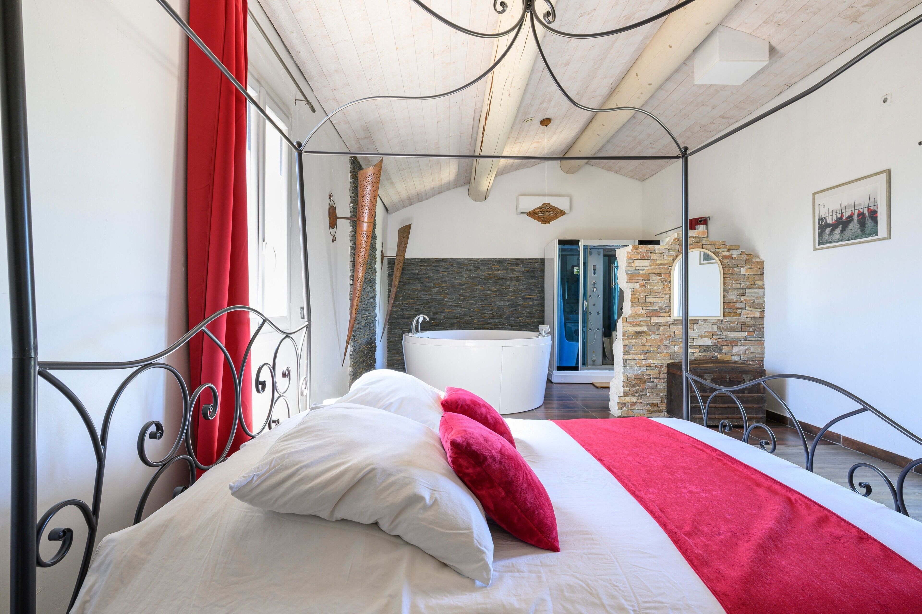 A bedroom with a bed, a red curtain, a bathroom with a bathtub, and a stone wall.