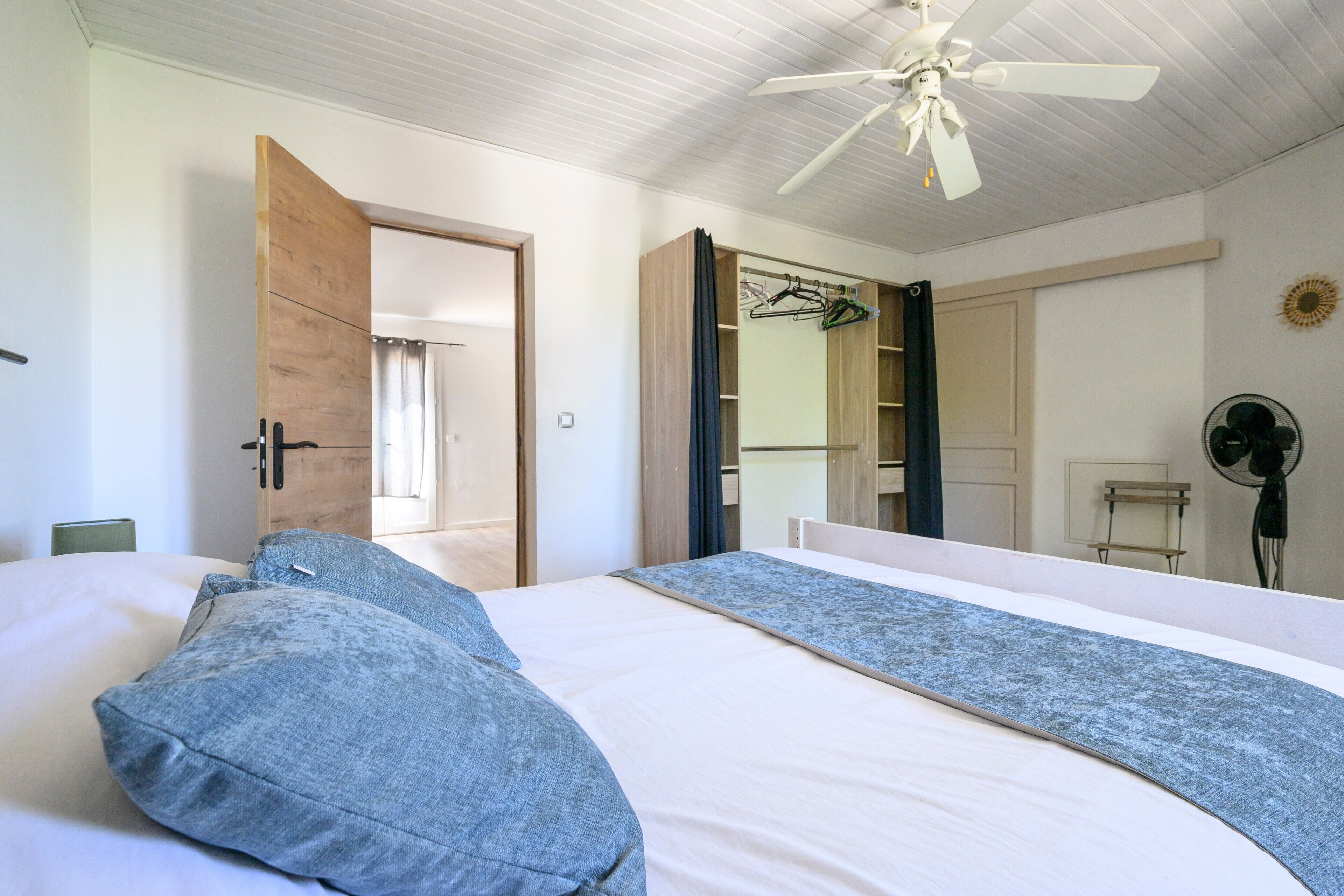 A bedroom with a bed, a ceiling fan, a wardrobe, and a mirror.