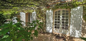 A covered outdoor area with white shutters, a tiled floor, and lush greenery. - House with garden and jacuzzi - near city center (Saint-Tropez)