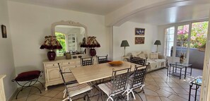 A dining area with a wooden table and chairs, a mirror, and a sofa with cushions. - House with garden and jacuzzi - near city center (Saint-Tropez)