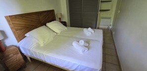 A neatly made bed with white linens and two rolled towels, a wooden headboard, a bedside table with a lamp, and a wardrobe in the background. - House with garden and jacuzzi - near city center (Saint-Tropez)