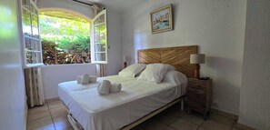 A neatly made bed with white linens and towels, a wooden headboard, a bedside table with a lamp, and a window with curtains. - House with garden and jacuzzi - near city center (Saint-Tropez)
