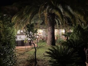 Ein beleuchteter Außenbereich bei Nacht mit Pool, Palmen und einem Gebäude im Hintergrund.
