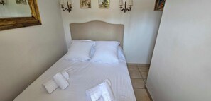 A neatly made bed with white linens and two pillows, a bedside table with a lamp, and a wall-mounted picture frame. - House with garden and jacuzzi - near city center (Saint-Tropez)