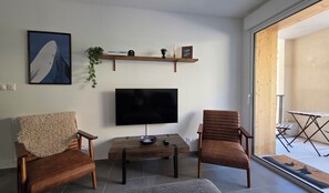 Ein modernes Wohnzimmer mit Flachbildfernseher, zwei Ledersesseln, einem Holztisch und einer kleinen Ablage mit Dekoration.