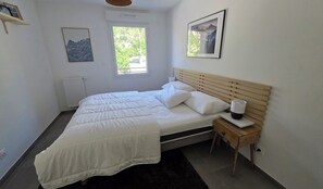 Ein Schlafzimmer mit einem Bett, einem Nachttisch mit Lampe, einem Heizkörper und zwei gerahmten Bildern an der Wand.