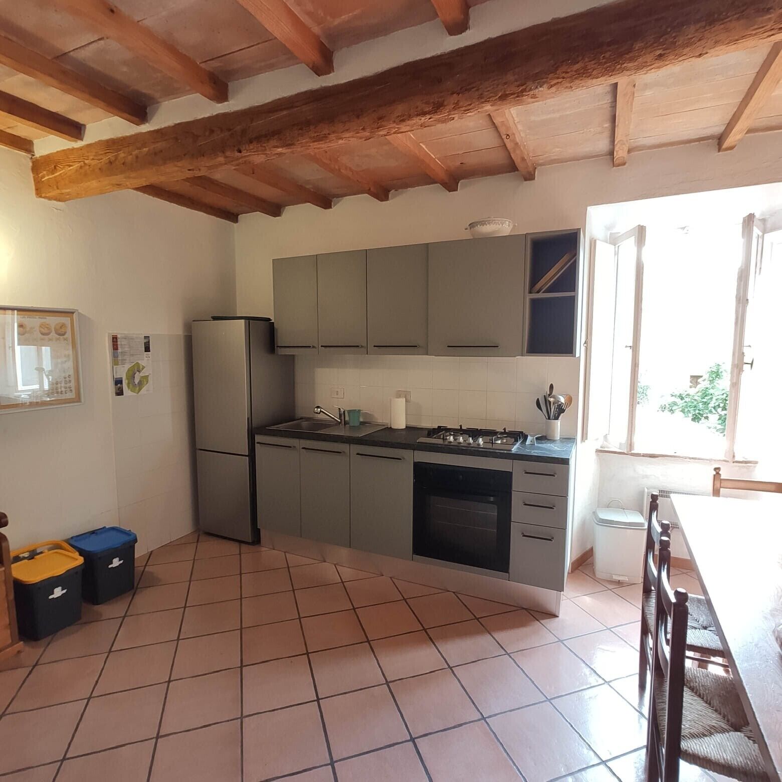 A kitchen with grey cabinets, a refrigerator, a stove, and a tiled floor.