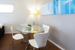 A modern dining area with a glass table, white chairs, a floor lamp, and a wall art piece. - Lovely 2BR Apartment in West Perth with Parking! (West Perth)
