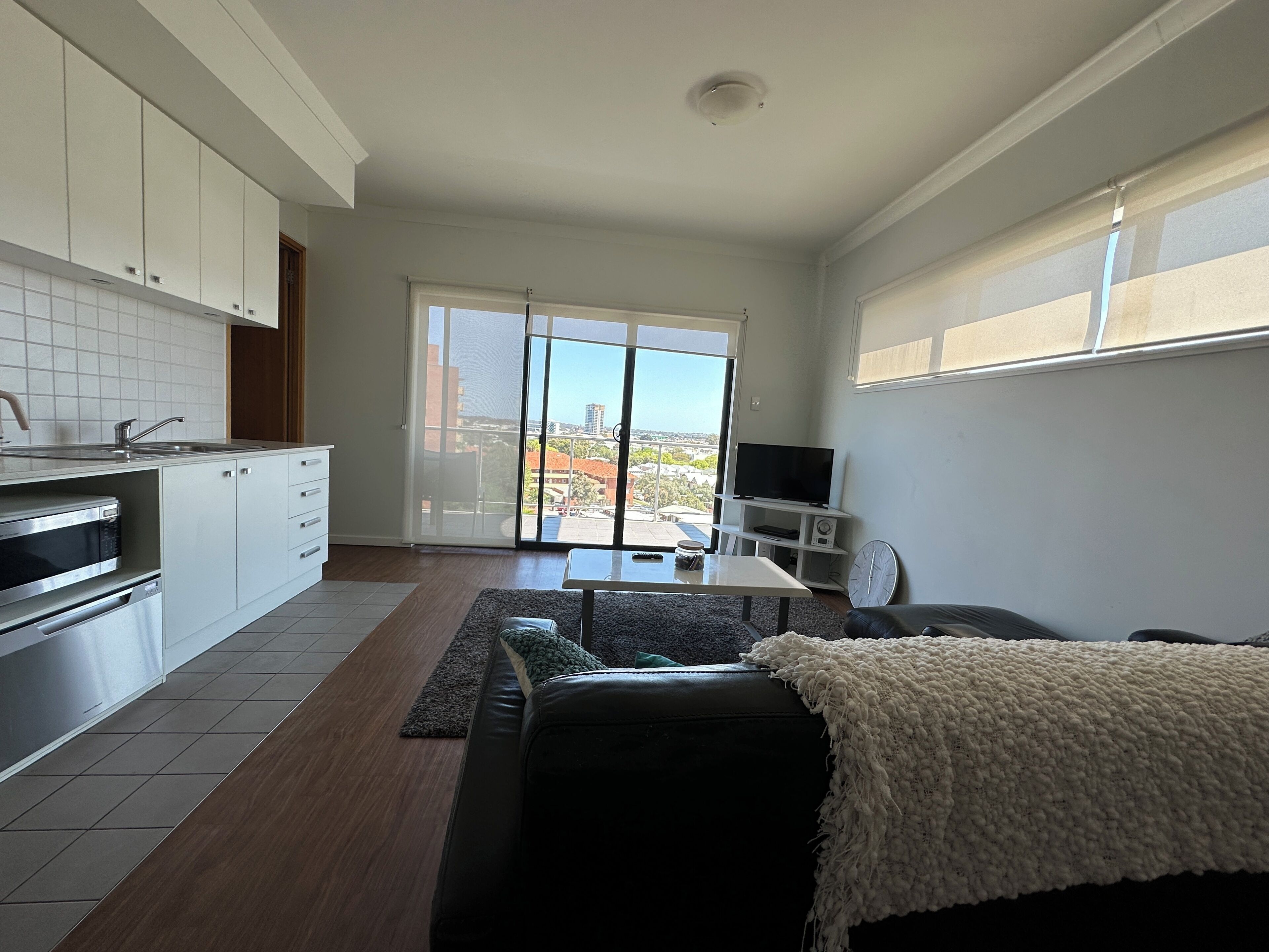 A modern kitchen with a built-in oven and microwave, a dining area with a table and chairs, and a sofa with a white throw blanket.