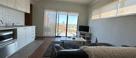 A modern kitchen with a built-in oven and microwave, a dining area with a table and chairs, and a sofa with a white throw blanket.