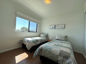 A bedroom with two beds, a window, and a wall-mounted picture. - Lovely 2BR Apartment in West Perth with Parking! (West Perth)