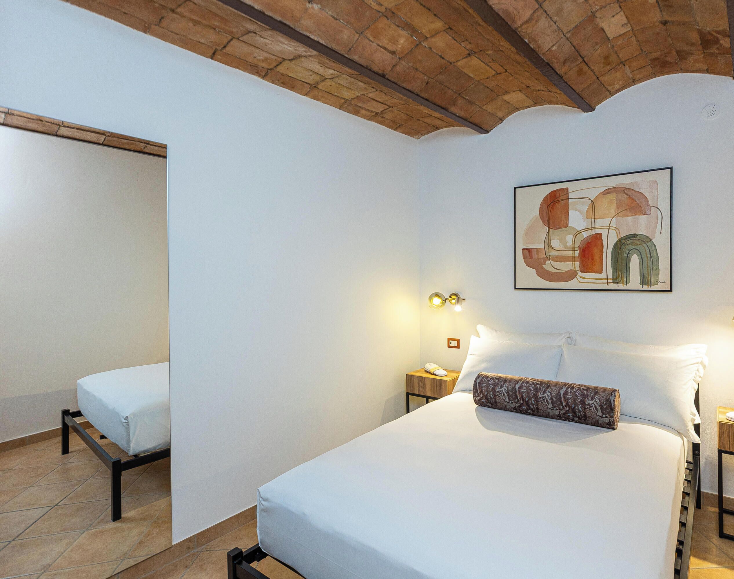 A hotel room with a bed, a bedside table with a lamp, and a painting on the wall.