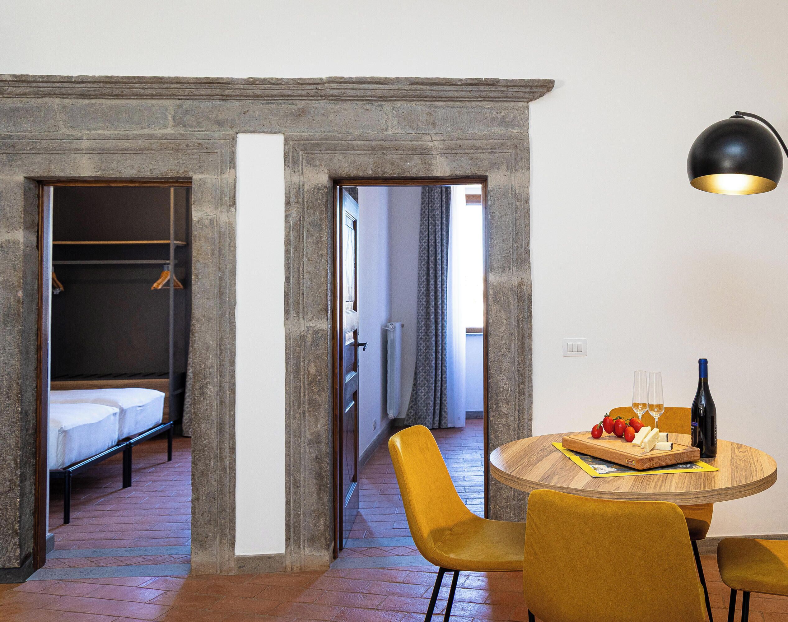 Ein Hotelzimmer mit einem Bett, einem runden Holztisch mit Flasche und Gläsern sowie einem gelben Stuhl.