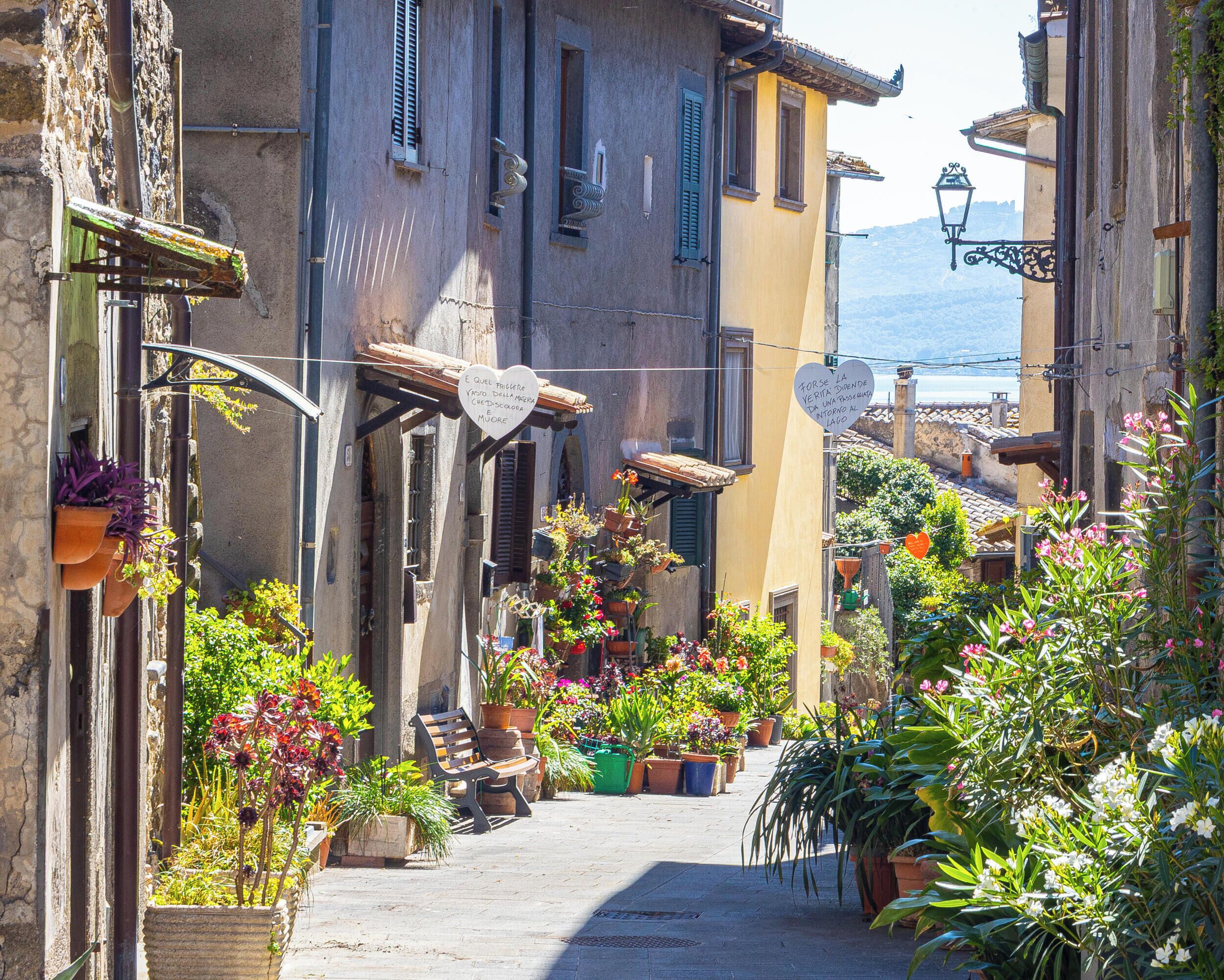 Une rue étroite, bordée de bâtiments des deux côtés, dont certains sont dotés de balcons et de plantes en pot.