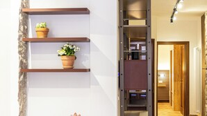 A hallway with a wooden floor, a staircase, and a wall-mounted shelf with potted plants.