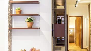 A hallway with a wooden floor, a staircase, and a wall-mounted shelf with potted plants.