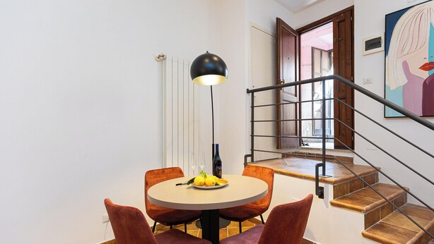 A dining area with a round table, four chairs, a floor lamp, and a bottle of wine.