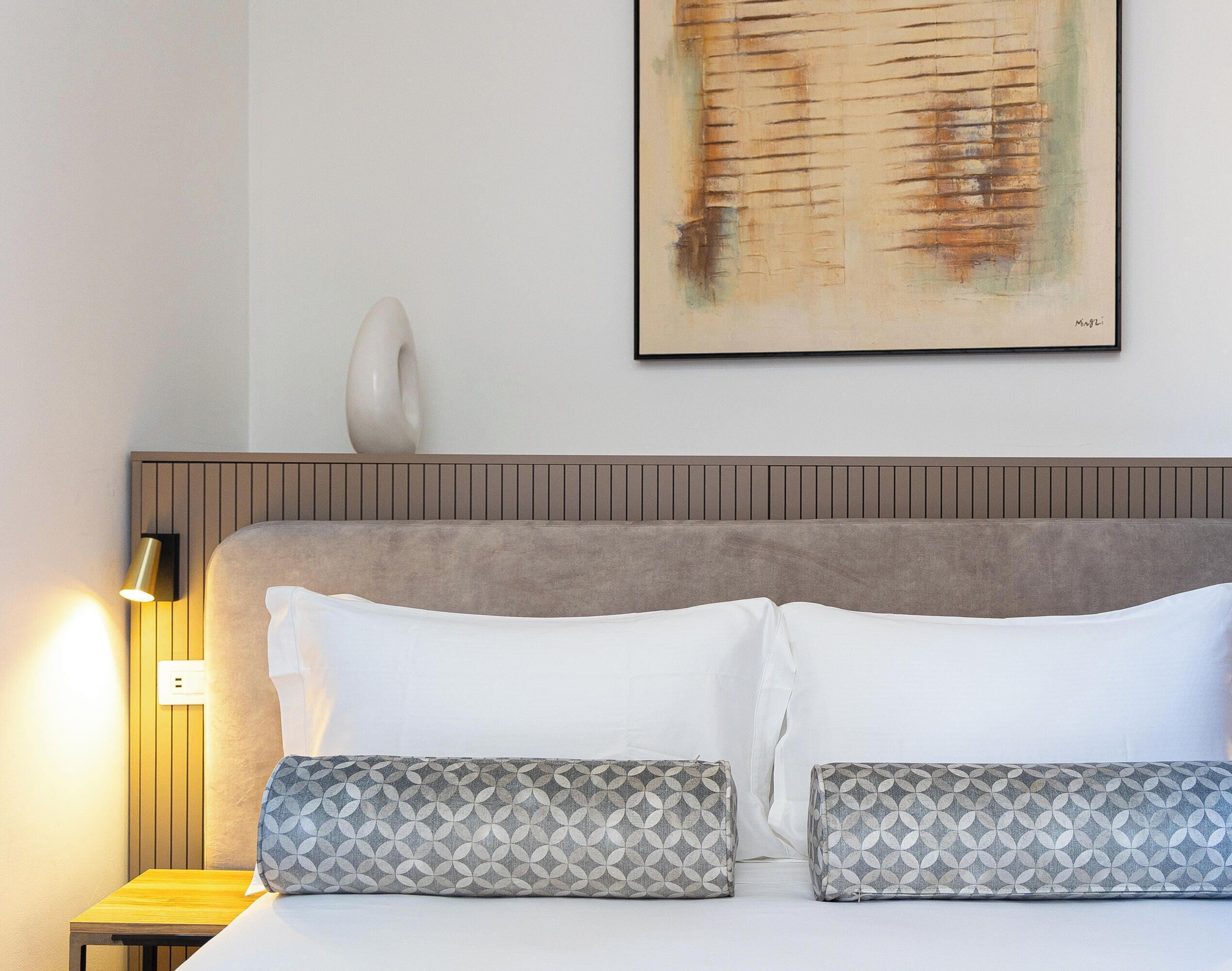 Une chambre d’hôtel avec un lit, des oreillers, une lampe fixée au mur et un tableau.