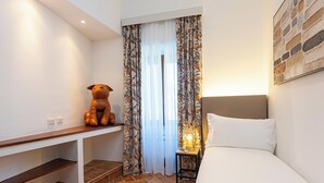 A hotel room with a bed, a desk, a lamp, and a teddy bear.