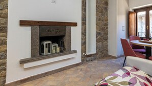 A room with a stone fireplace, a radiator, a dining area with a table and chairs, and a patterned rug.