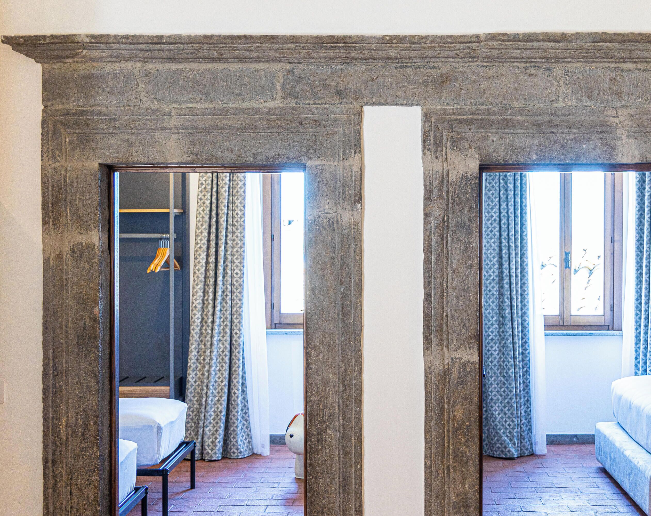 A room with a stone wall, a bed, a bench, and a hanging coat rack.
